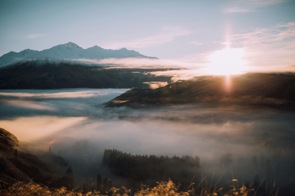 A sunrise over mountains with foggy ground below the peaks of the mountains