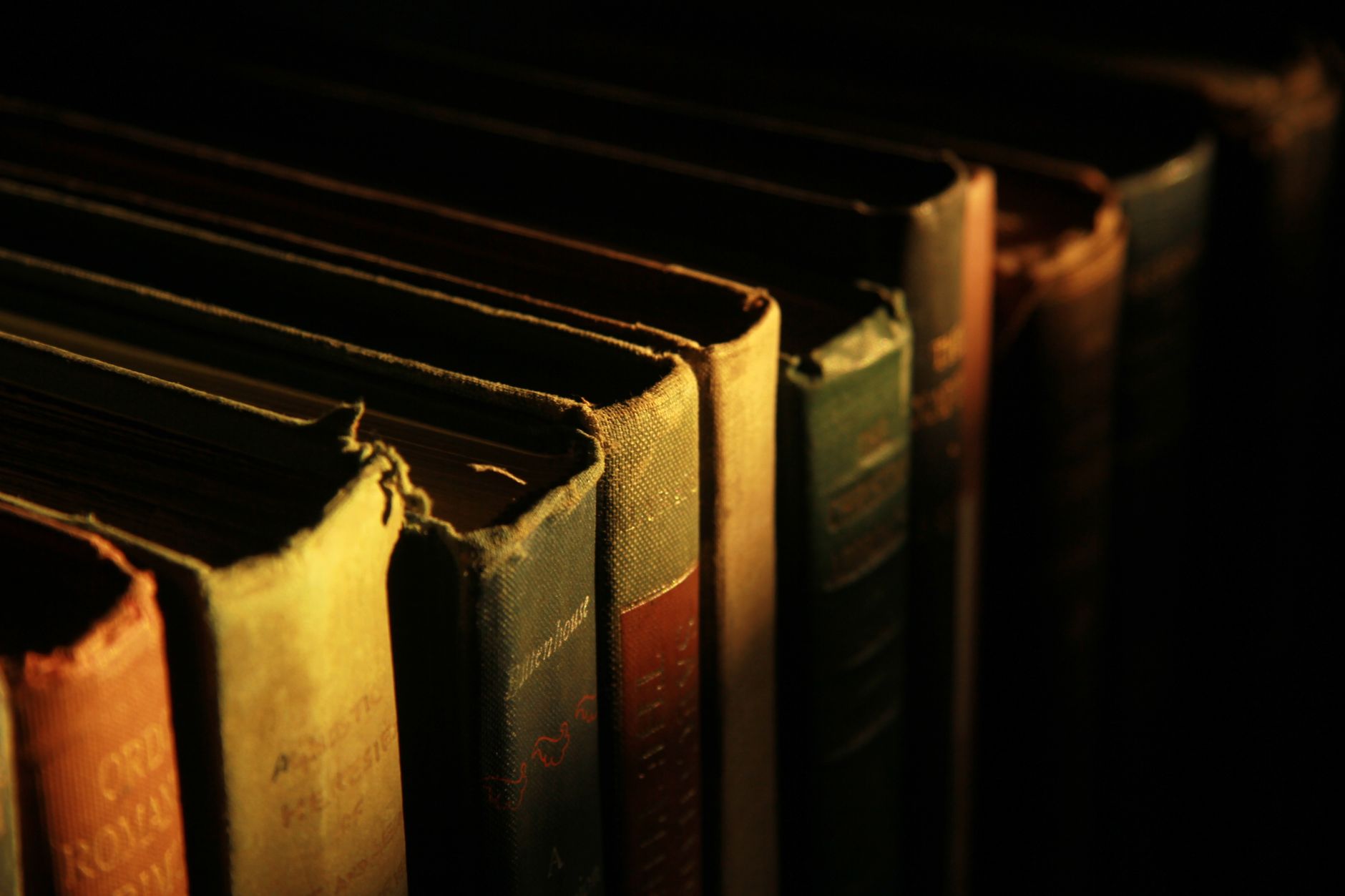 A picture showing the tops and part of the spines of various old hardback books, with low lighting.